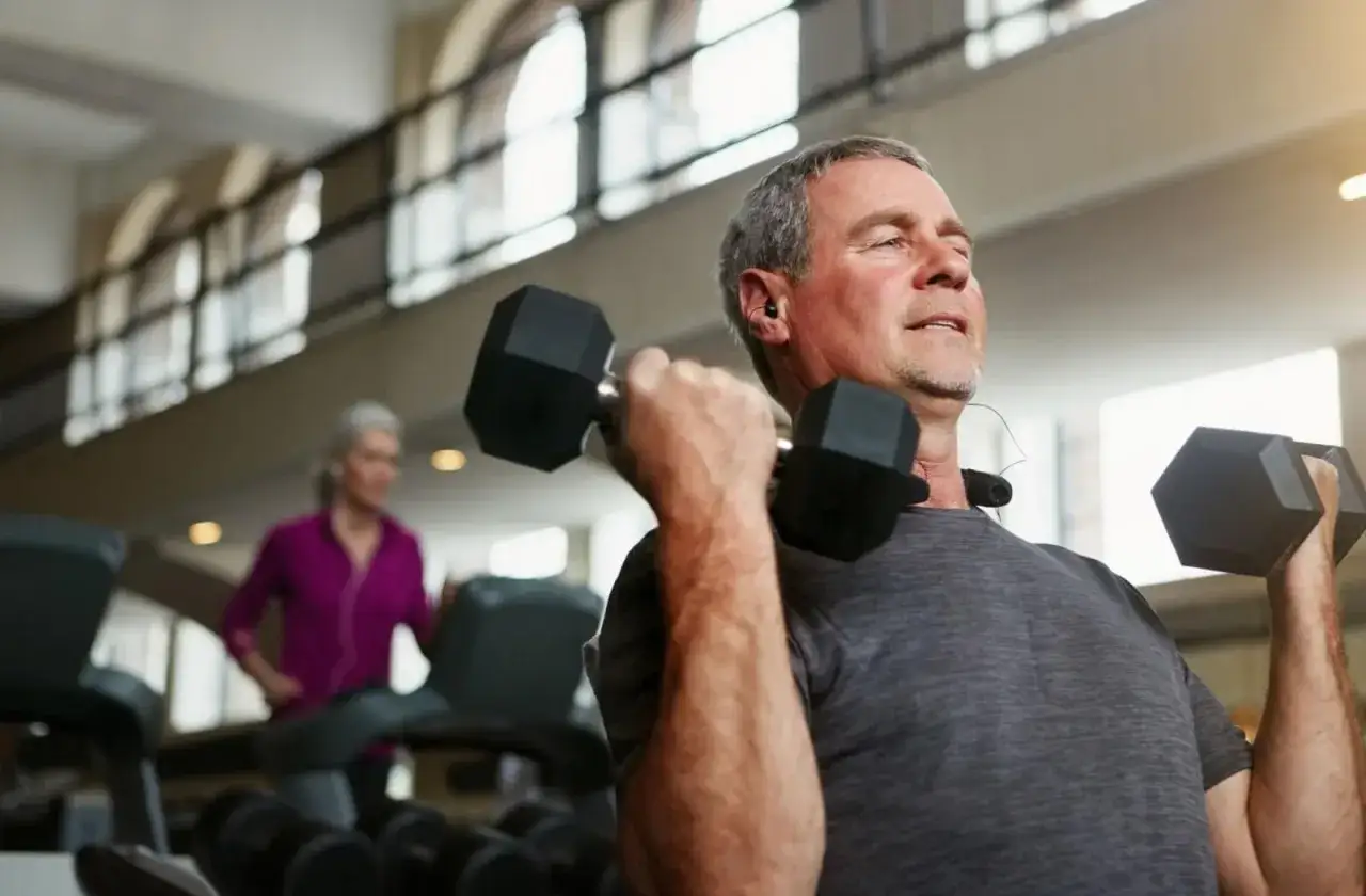 Uomo anziano solleva pesi in palestra, combattendo la sarcopenia cos'&egrave;. Allenamento per mantenere la forza muscolare.