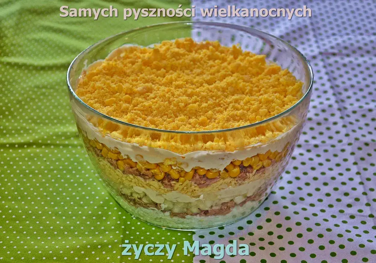 Warstwowa sałatka z tuńczykiem, kukurydzą i jajkiem, posypana żółtym sypkim składnikiem. Idealna na wielkanocny stół.
