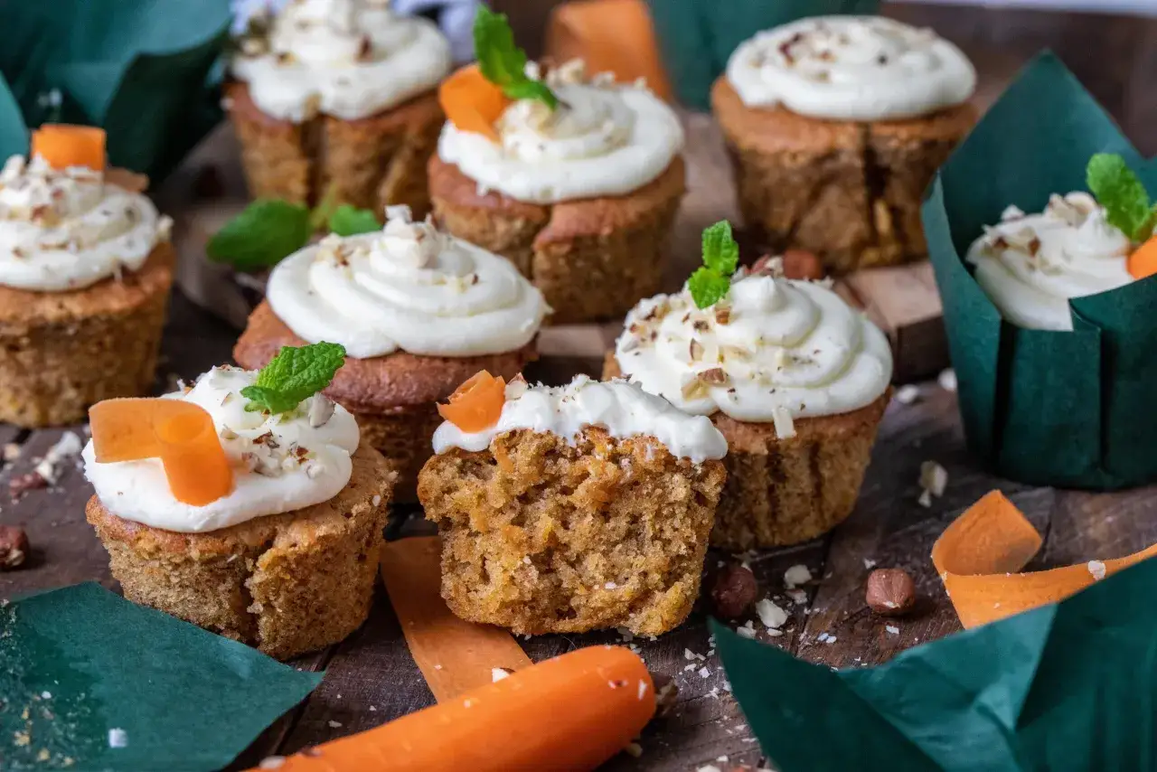 Fluffiga morotskaka muffins med krämig frosting, toppade med nötter och en liten morotsdekoration. Perfekta för fikat!