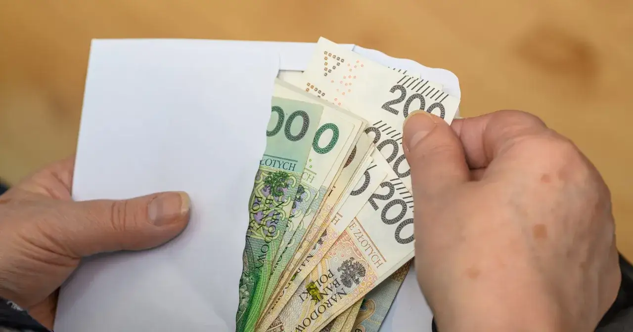 Dłonie trzymają kopertę z polskimi banknotami. Czy to najwyższa emerytura w Polsce?