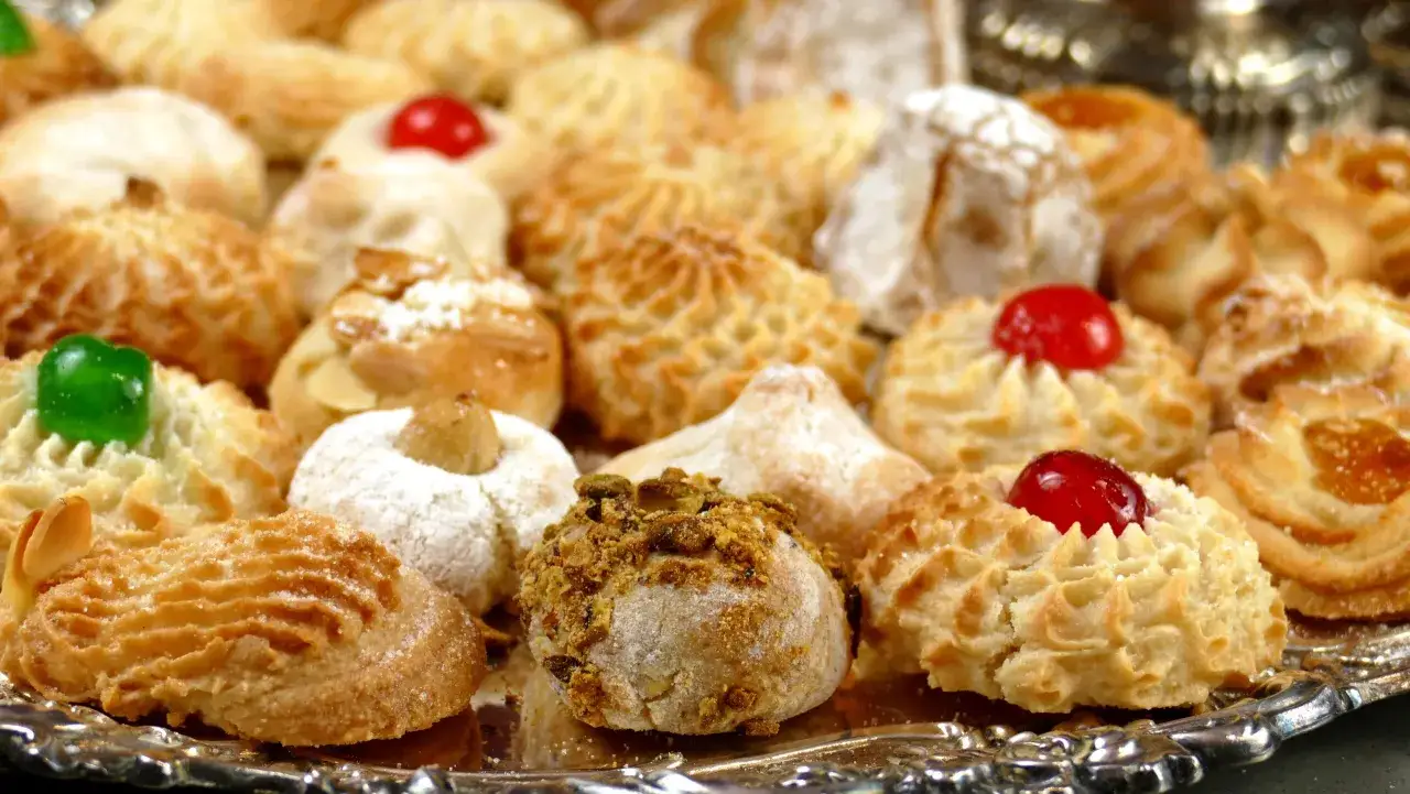 Vassoio pieno di biscotti con farina di mandorle, alcuni decorati con ciliegie candite, mandorle e pistacchi.