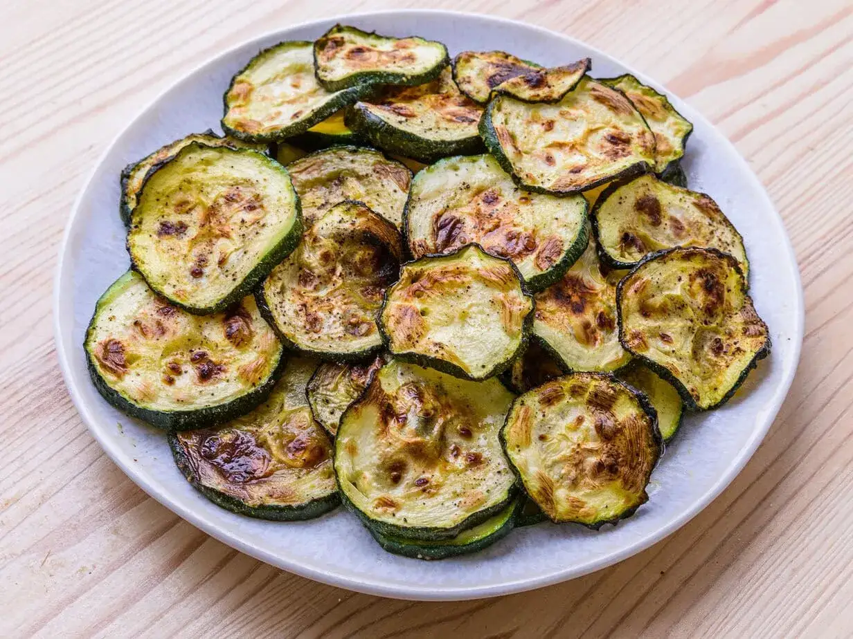 Tranches de courgette grillées à l'air fryer, légèrement dorées et assaisonnées, présentées sur une assiette blanche.