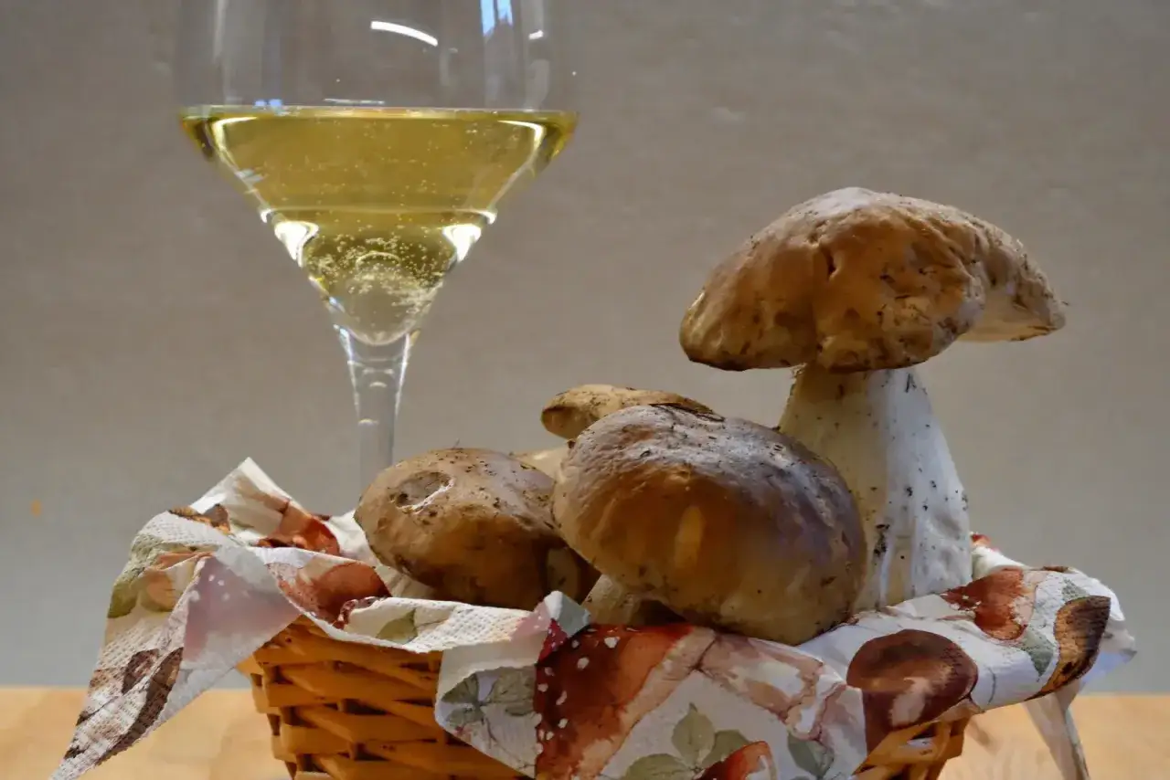 Un bicchiere di vino bianco frizzante e funghi porcini freschi in un cestino, un perfetto abbinamento vino funghi per un'esperienza culinaria.
