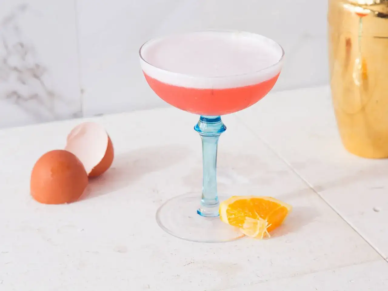 Ein cremiger Campari Sour mit Eierschale und Orangenspalte, bereit zum Genuss.