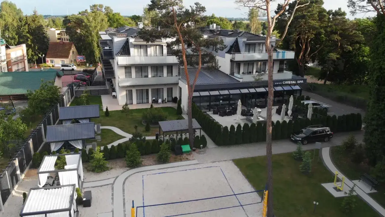 Nowoczesny hotel Cristal Spa z basenem i kortem do siatkówki plażowej, otoczony zielenią.