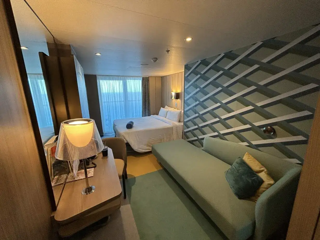 Ecco cosa trovo in cabina Costa Crociere: letto comodo, divanetto, scrivania con lampada e un muro decorato.
