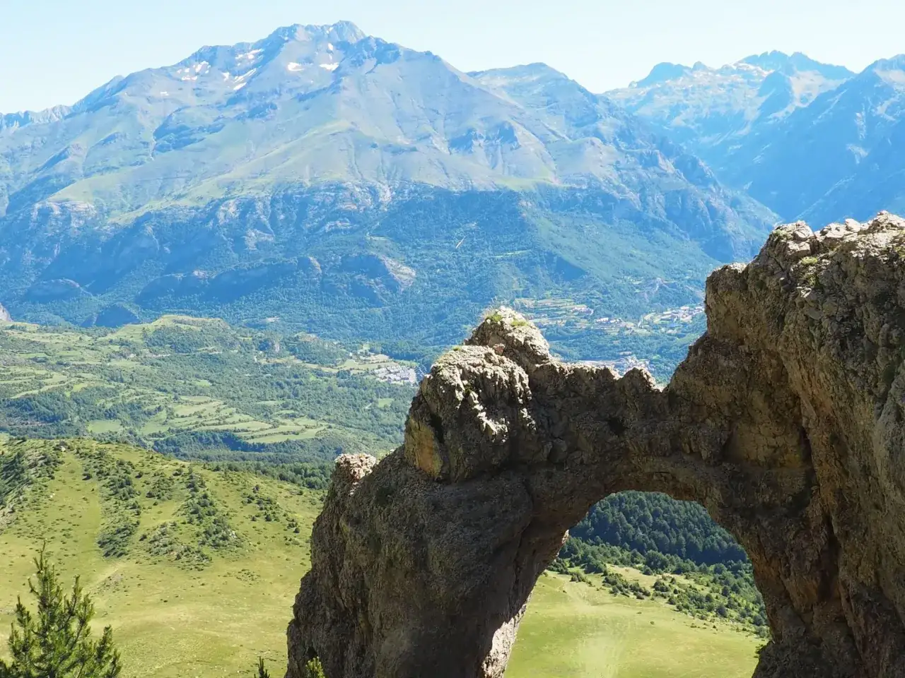 Arco natural de roca en el **Valle de Tena**, con vistas a monta&ntilde;as y prados verdes.
