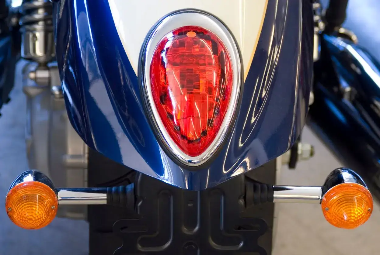 Detalle de la parte trasera de una moto azul y blanca, con intermitentes naranjas y luz roja. Podr&iacute;a ser una multa por llevar luces led moto.