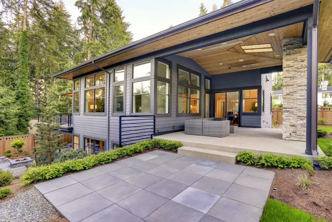 Maison moderne avec terrasse et finition dalle béton. Le jardin est aménagé avec des arbustes et des graviers.