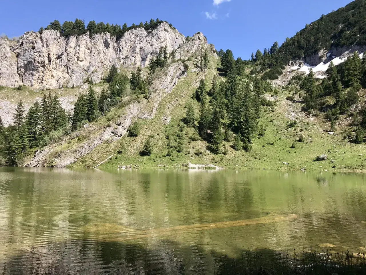 Eine malerische kosovo landschaft mit einem ruhigen See, der von steilen, felsigen Bergen und gr&uuml;nen H&auml;ngen mit Nadelb&auml;umen ges&auml;umt ist.