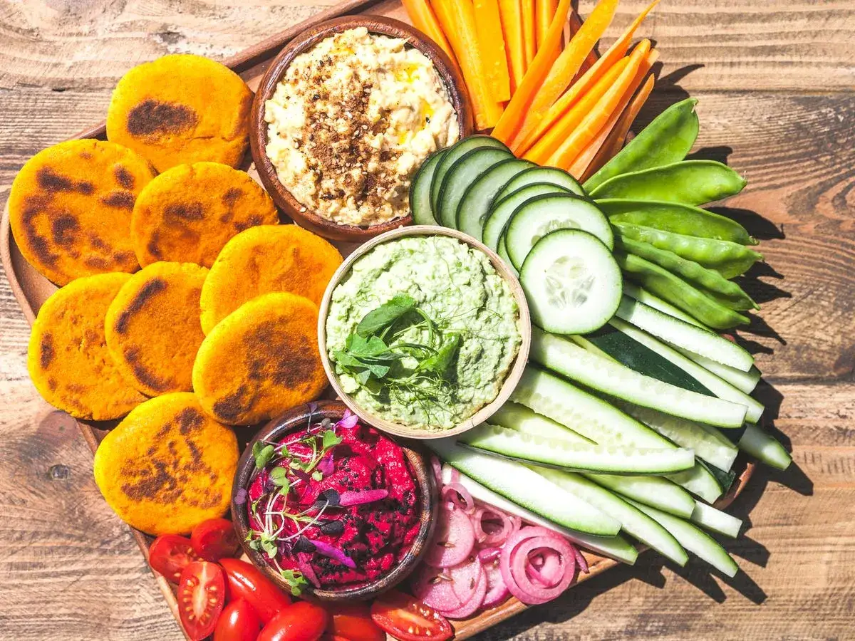 Bunte Gemüse-Dips mit Hummus, Guacamole und Rote Bete, dazu Karotten-, Gurken- und Zuckerschoten-Sticks sowie kleine Maisfladen. Perfekt, was satt macht und wenig Kalorien hat.