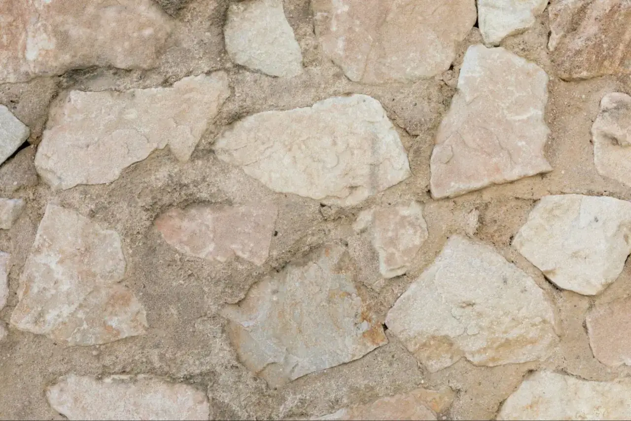 Mur en pierres naturelles irrégulières, avec des variations de couleurs allant du beige rosé au gris. Idéal pour apprendre comment enlever des taches sur de la pierre naturelle.