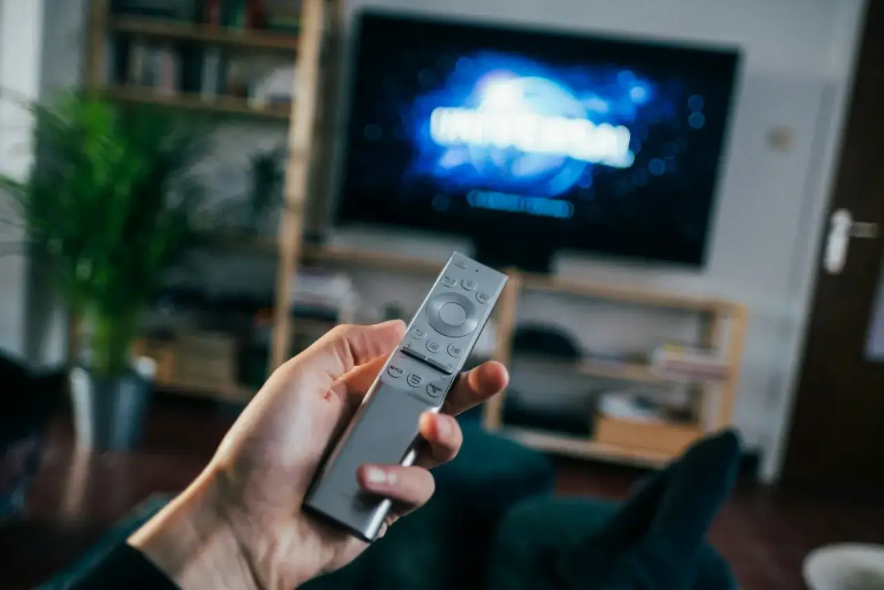Dłoń trzymająca pilot do telewizora, na ekranie logo Universal. Szukasz sposobu, jak wyłączyć lektora dla niewidomych?