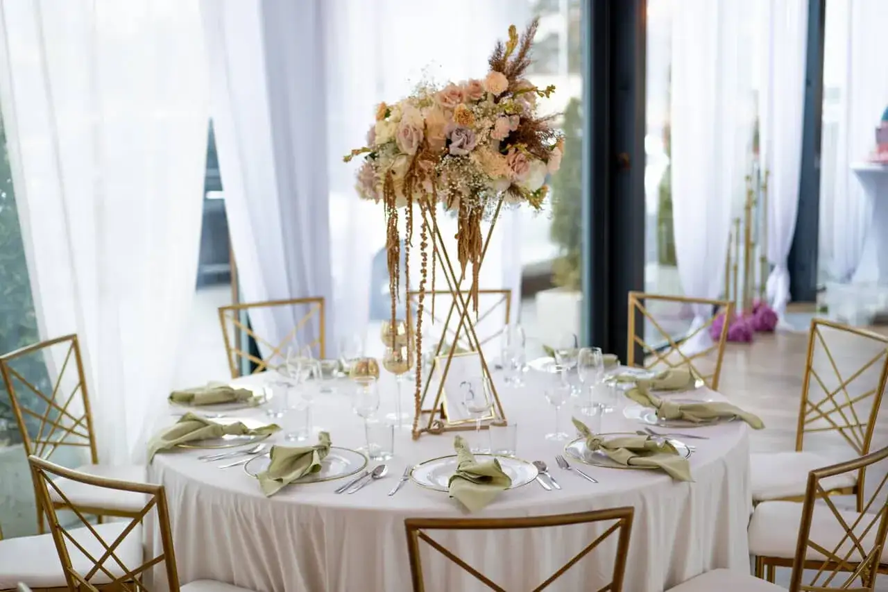 Elegancko nakryty stół weselny z bukietem pastelowych kwiatów i złotymi krzesłami. Idealne miejsce na slow wedding.