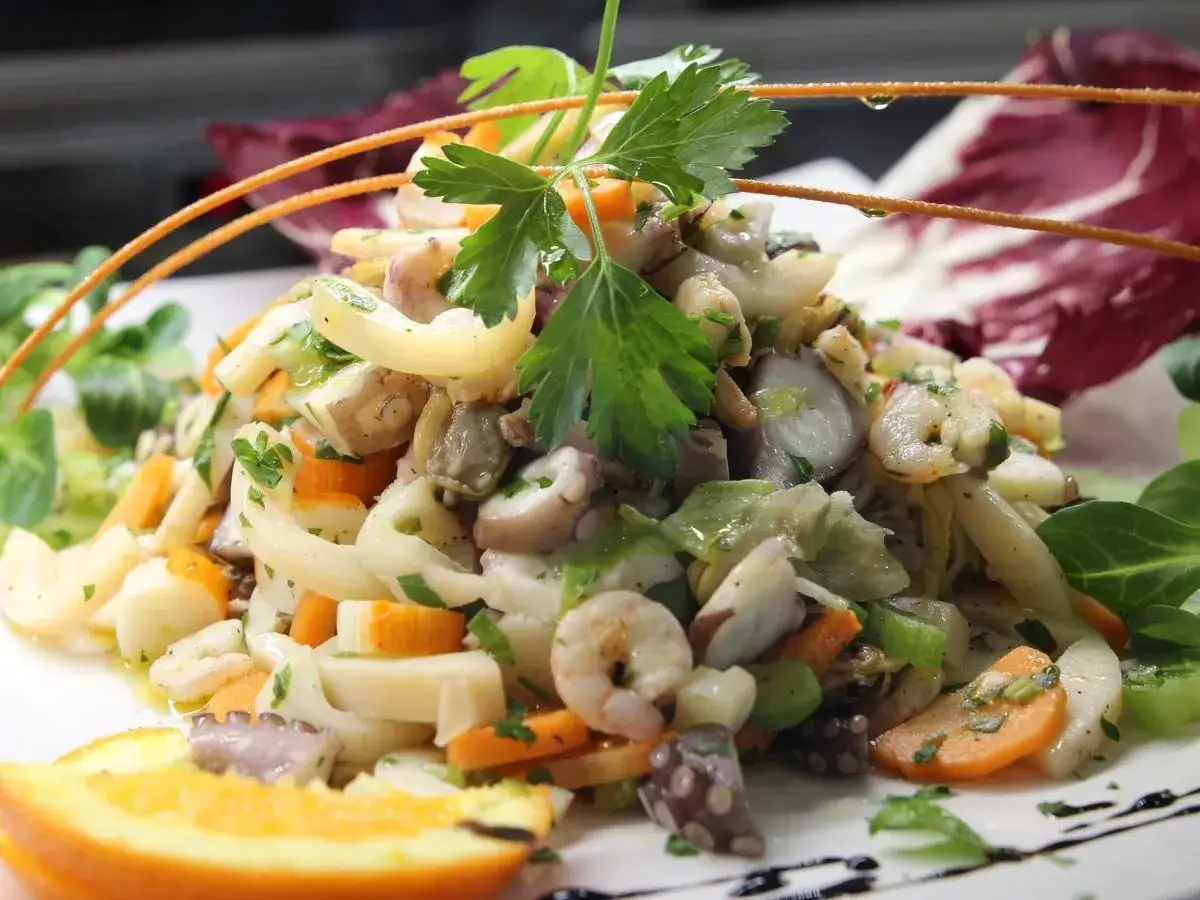 Frischer insalata di mare mit Oktopus, Garnelen, Karotten und Kräutern, garniert mit Orangenspalte und Radicchio.