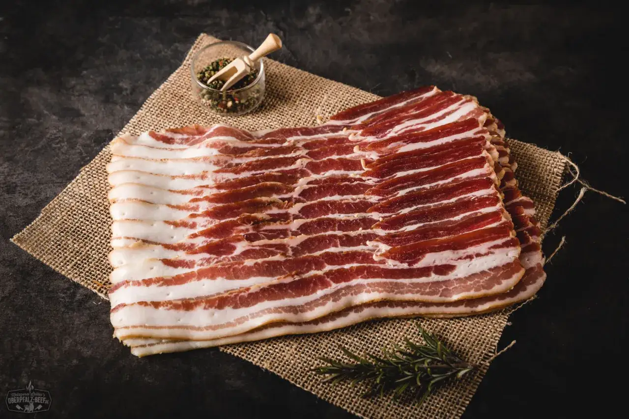 Frisch geschnittener Speck, perfekt f&uuml;r smoker rezepte schwein. Daneben eine kleine Schale mit Pfefferk&ouml;rnern und ein Rosmarinzweig.