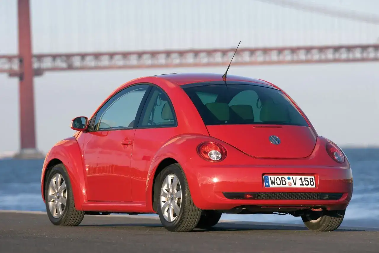 Czerwony, nowy Beetle z charakterystycznym kształtem, zaparkowany przy moście.