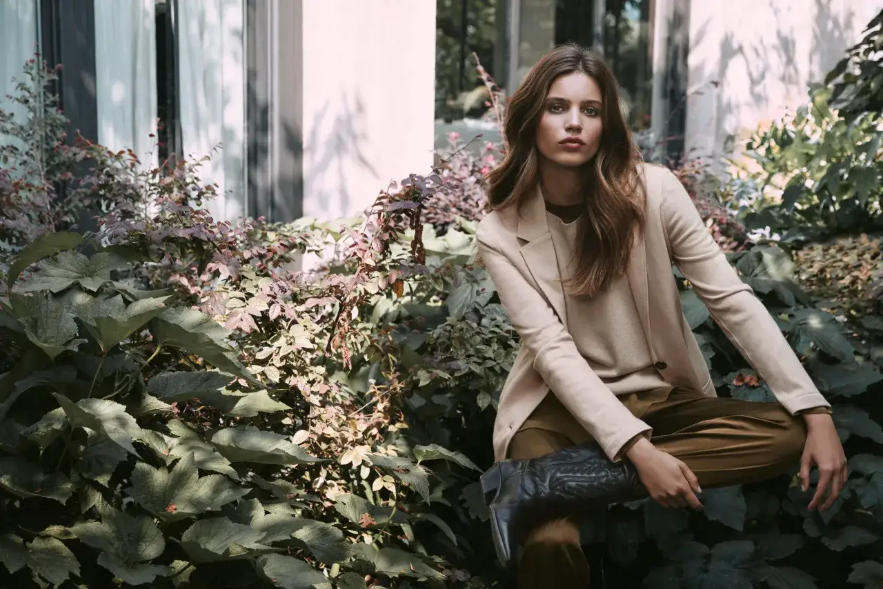 Donna di 45 anni con un outfit chic: blazer beige, pantaloni color kaki e stivali texani neri.