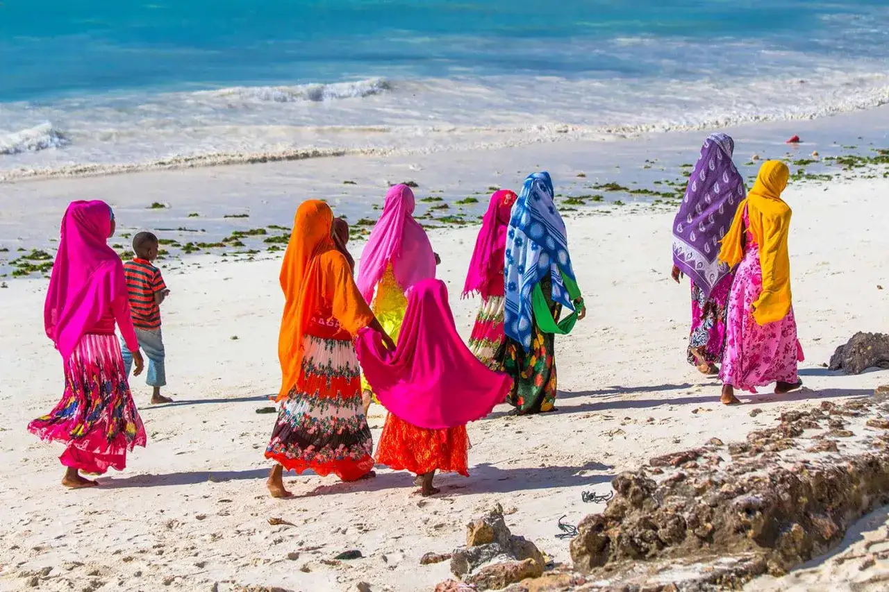 Kolorowe kobiety w tradycyjnych strojach spacerują po plaży, odkrywając zanzibar atrakcje.