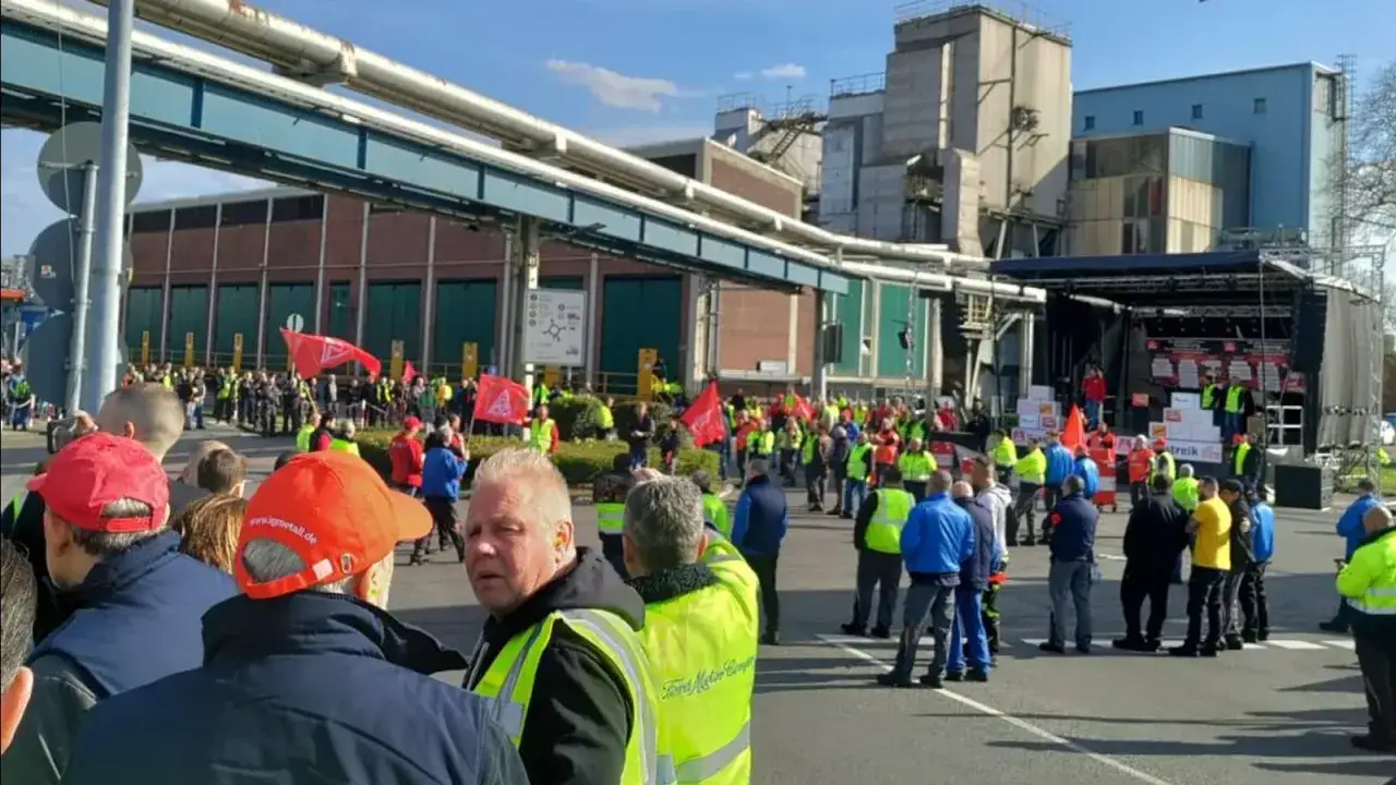 Demonstranten vor Ford-Werk fordern faire Abfindung. Rote Fahnen und Warnwesten pr&auml;gen das Bild.