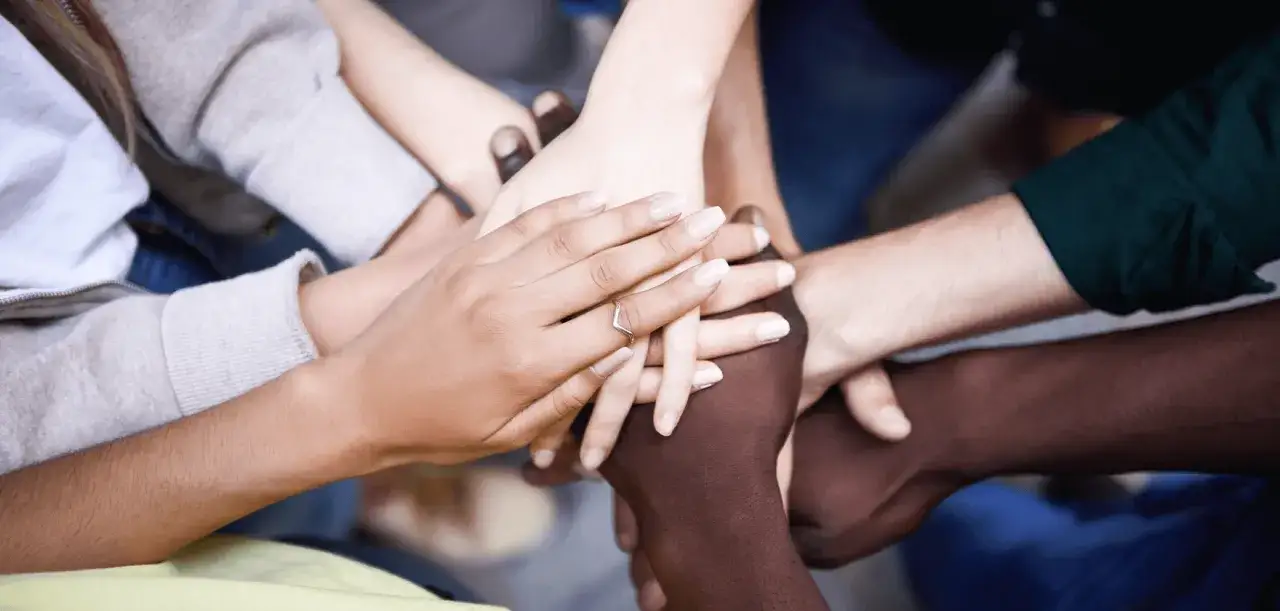 A diverse group of hands stacked together, symbolizing unity and support. This image asks the question: does God love gay people?
