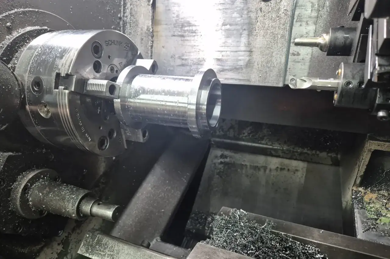 Precyzyjna produkcja CNC: tokarka obrabia metalowy element, wióry metalowe świadczą o pracy maszyny.