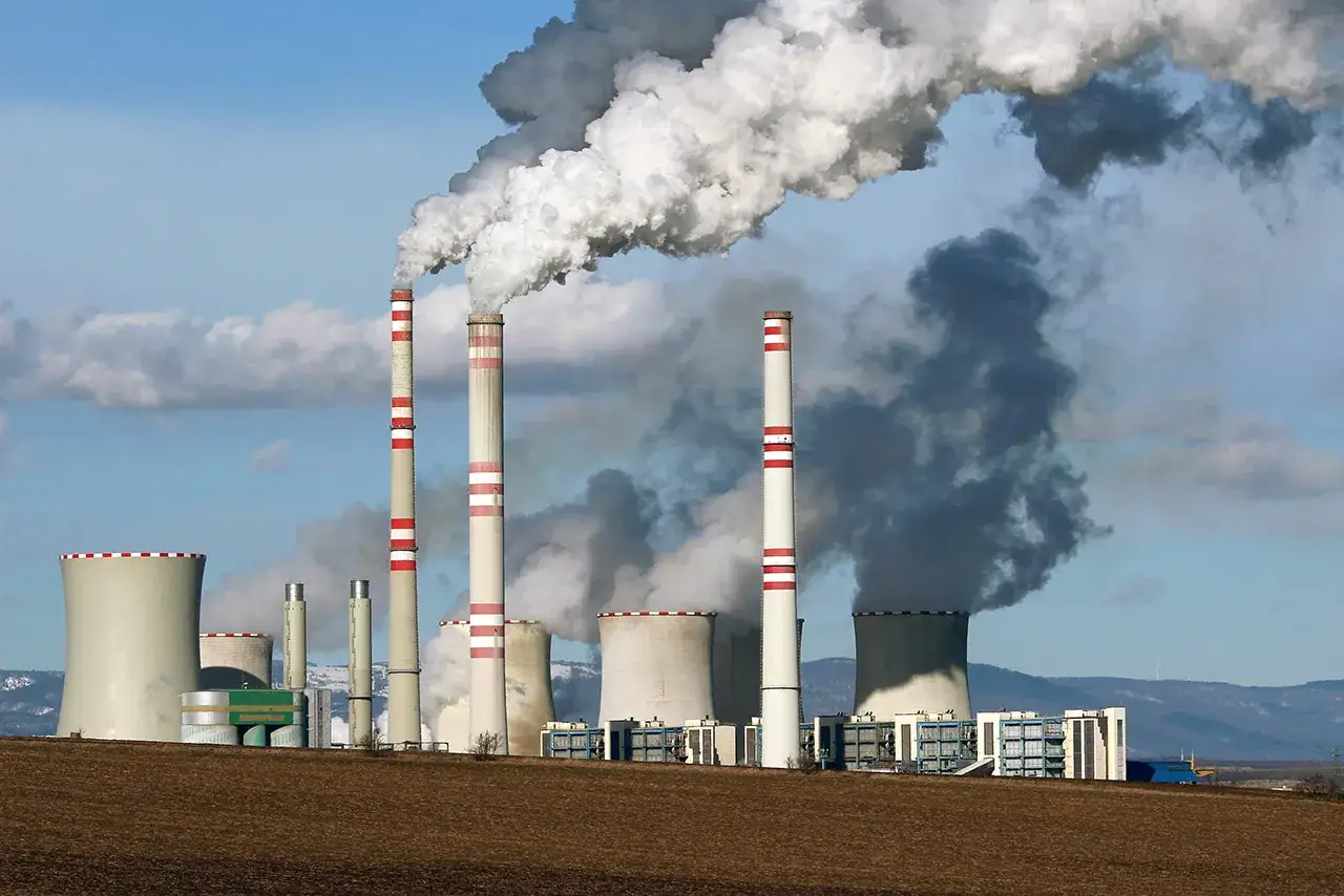 Dymiące kominy elektrowni, chmury pary wodnej unoszą się w powietrze. Choć nie widać tego bezpośrednio, proces ten może wiązać się z emisją promieniowania jonizującego.