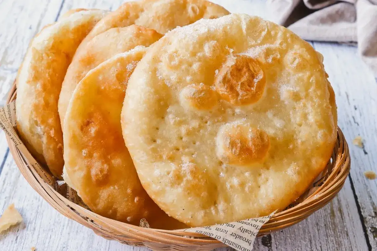Buñuelos de viento dorados y esponjosos, espolvoreados con azúcar, servidos en una cesta de mimbre.