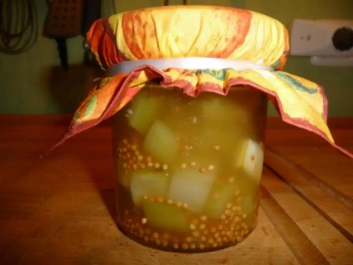 Glas mit eingelegten Gurken, Senfkörnern und einem bunten Stoffdeckel. Ein leckeres honiggurken rezept zum Nachmachen.