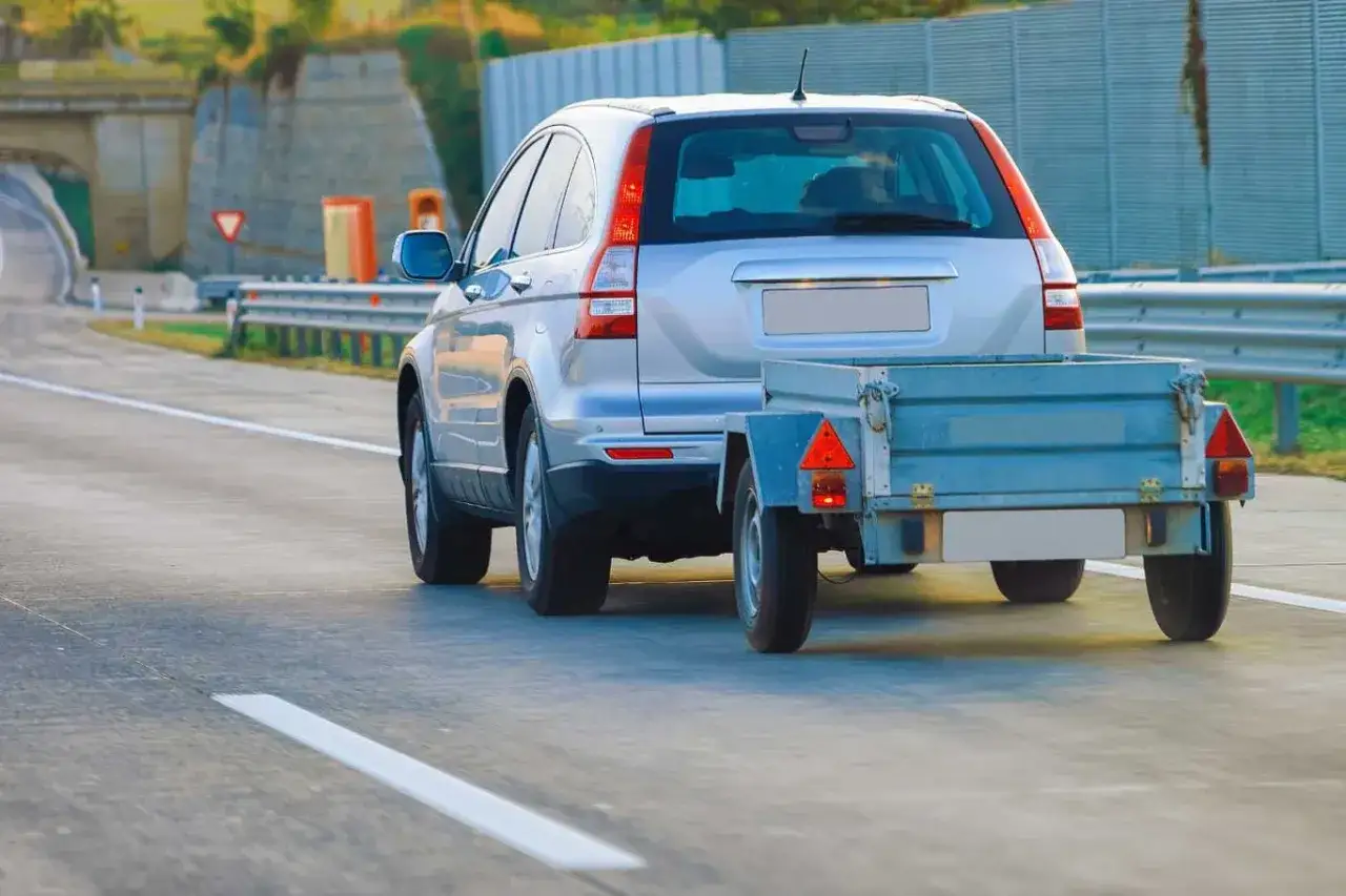 Srebrny SUV z przyczepką na drodze. Jazda z przyczepą to ważna umiejętność, często wymagana do uzyskania odpowiedniej kategorii prawa jazdy.