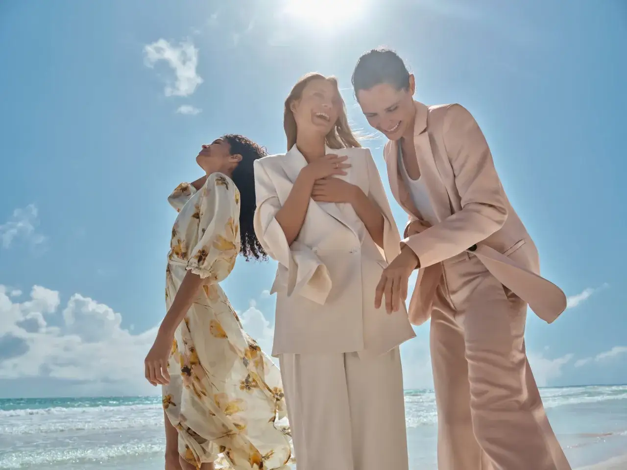 Drei Frauen in eleganter Abschlussfeier Kleidung Eltern am Strand. Eine tr&auml;gt ein gebl&uuml;mtes Kleid, die anderen schicke Hosenanz&uuml;ge.