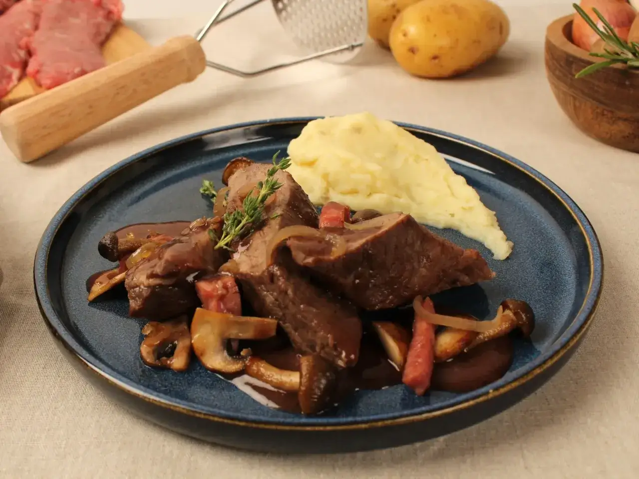 Pluma de porc recette : viande braisée, champignons, oignons et purée de pommes de terre sur une assiette bleue.