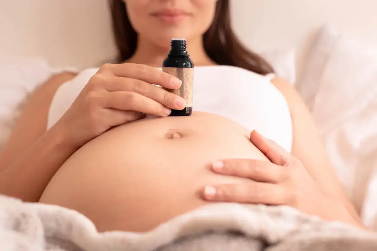 Une femme enceinte tient une petite bouteille d'huile essentielle sur son ventre.