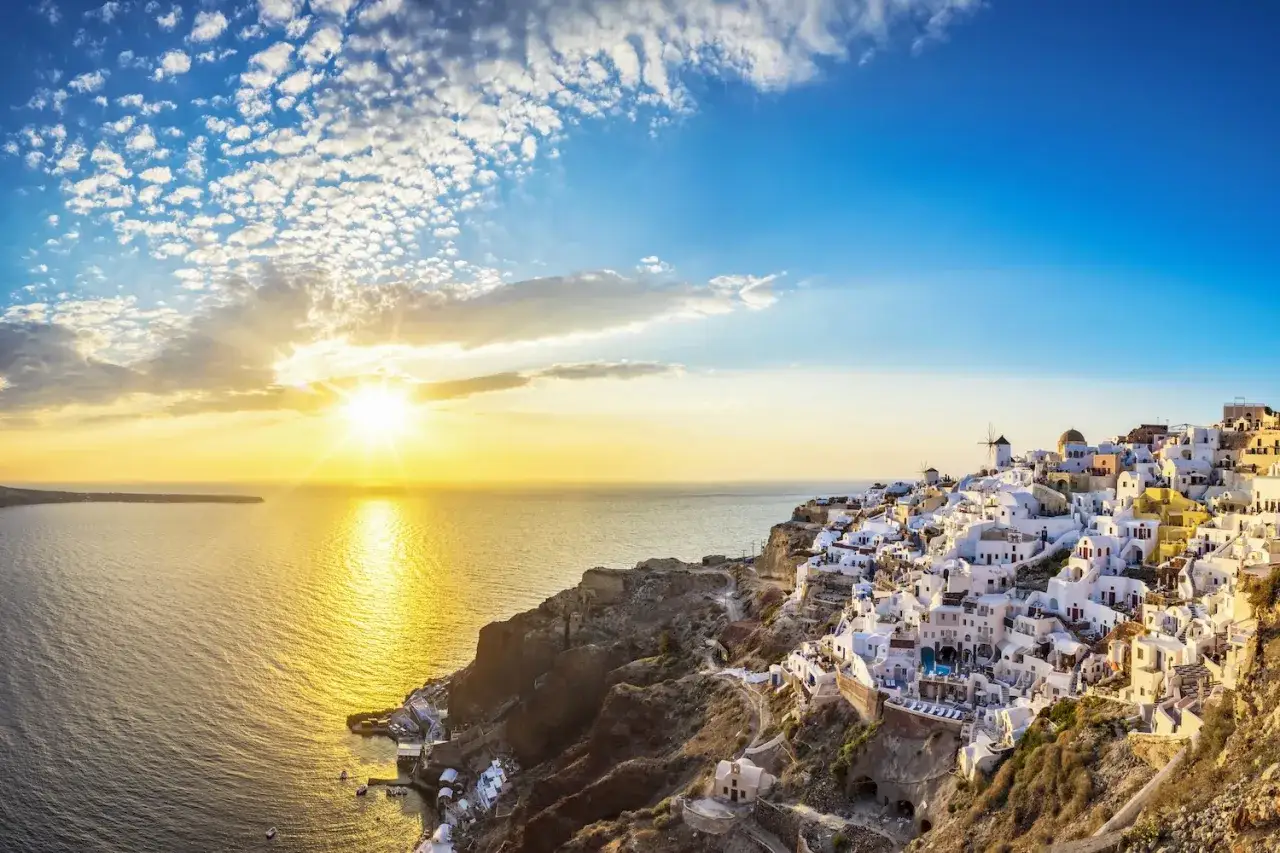 Zachód słońca nad Santorini, idealne miejsce na wakacje. Białe domki na klifie, błękitne morze i złote niebo tworzą niezapomniany widok.
