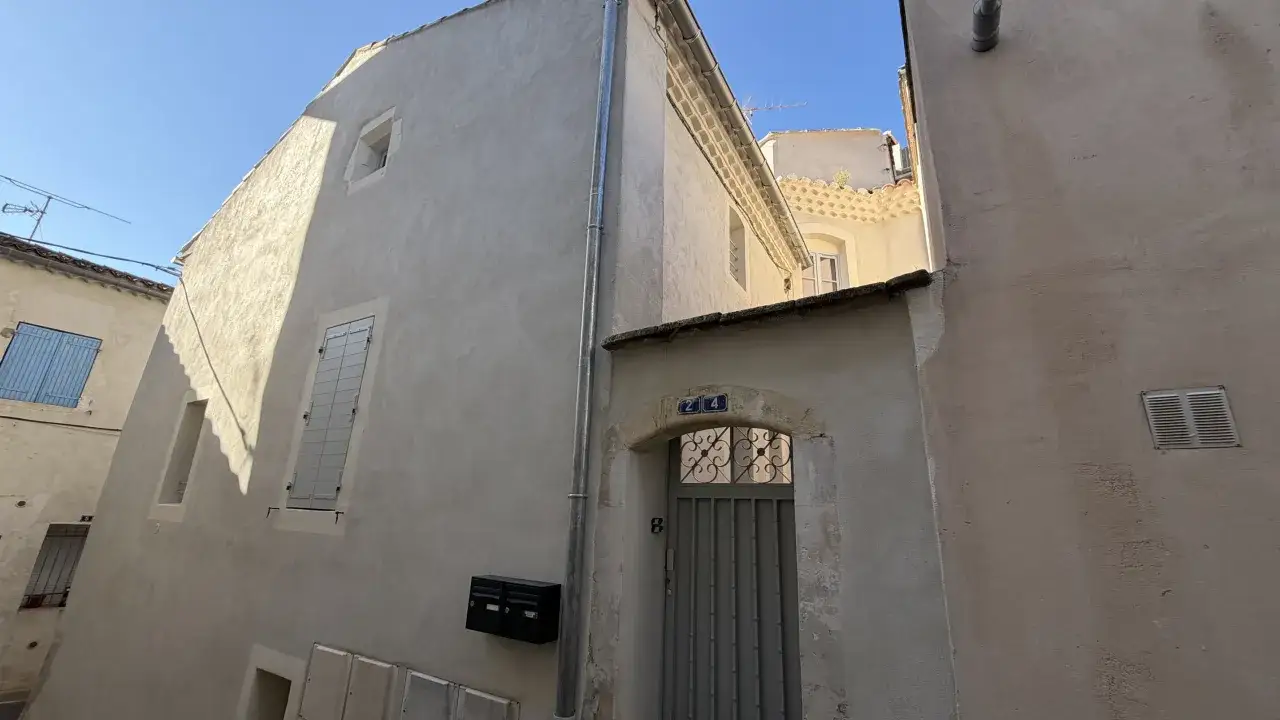 Façade d'une maison ancienne, idéale pour un projet SCPI déficit foncier. Fenêtres, volets bleus, boîtes aux lettres et porte ornée d'une plaque 