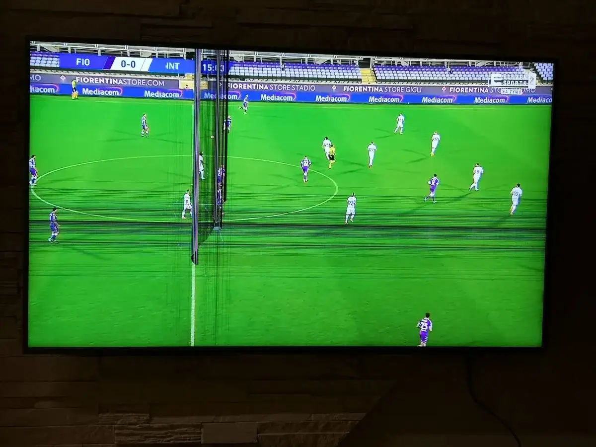 Uszkodzona matryca w telewizorze podczas meczu. Pionowe pasy zakł&oacute;cają obraz, ale widać piłkarzy na zielonej murawie.