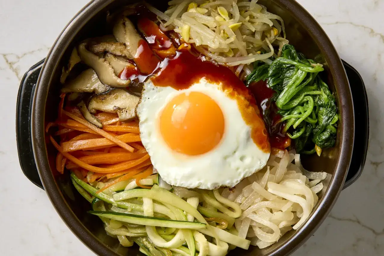 Bibimbap z jajkiem sadzonym, grzybami, marchewką, szpinakiem i kiełkami fasoli. Idealne danie z kuchni koreańskiej, które można łatwo przygotować według prostych przepisów.