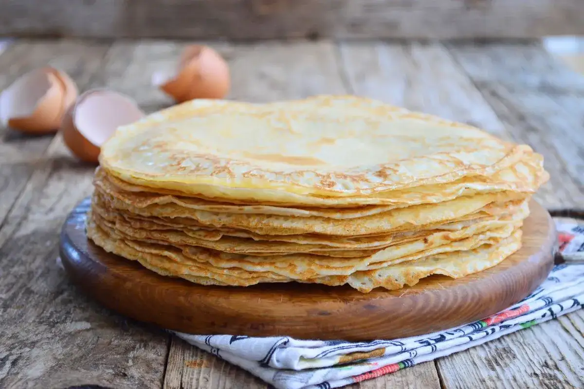 Pila di crepes senza burro dorate e sottili, pronte per essere farcite. Sullo sfondo, gusci d'uovo vuoti.