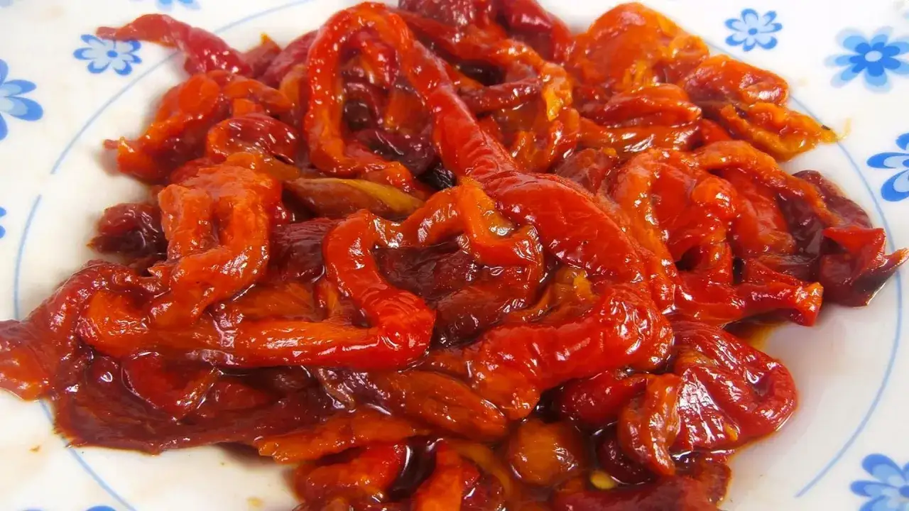 Pimientos asados, jugosos y brillantes, servidos en un plato blanco con un borde azul.