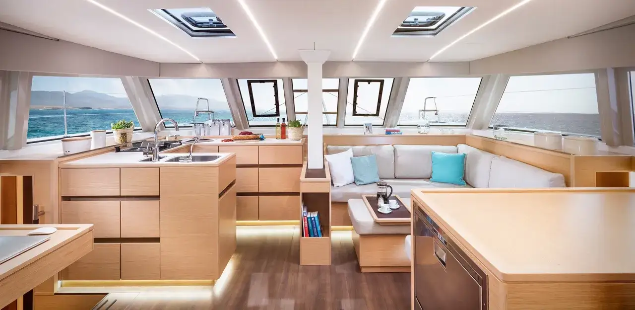 Interni luminosi di un catamarano con cucina attrezzata e comodo salotto, vista mare.