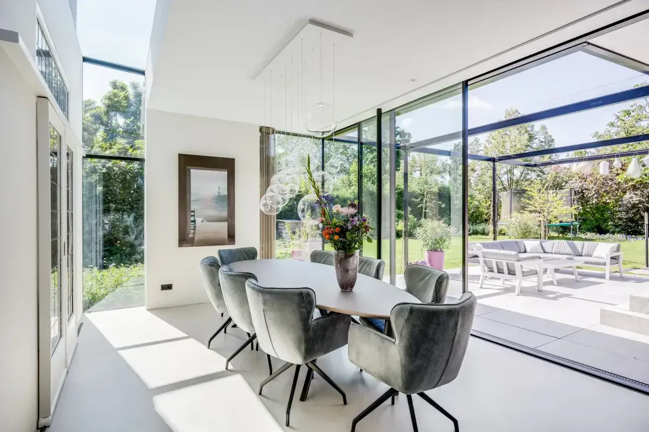 Een lichte, moderne eetkamer met grote ramen die uitkijken op de tuin. De eettafel is omringd door comfortabele stoelen, wat een uitnodigende vestibule creëert.