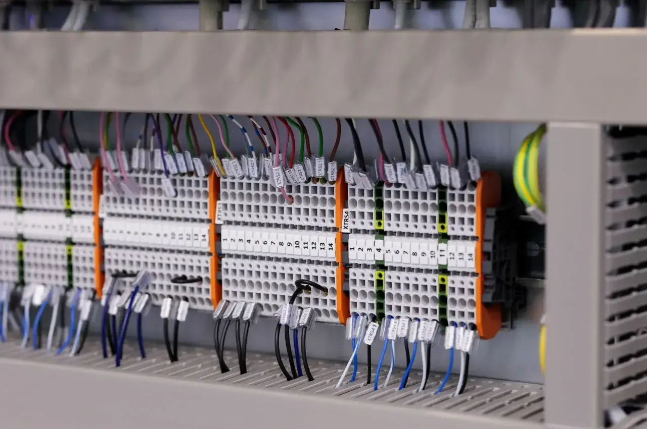 Panel sterowania z licznymi przewodami podłączonymi do zacisków. Widać oznaczenia, np. XTRS4, sugerujące system PLC.