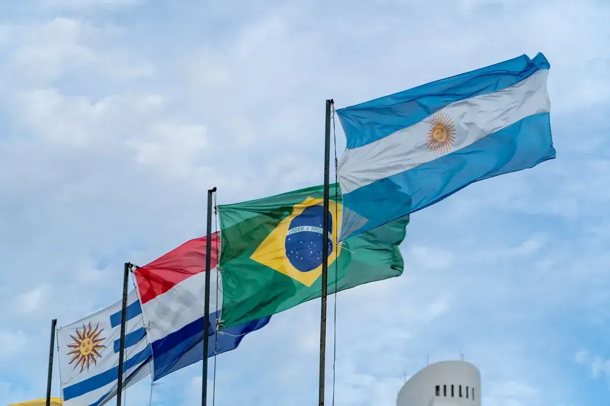 Flagi Argentyny, Brazylii, Urugwaju i Paragwaju powiewają na wietrze, symbolizując jedność i współpracę w ramach Mercosur. Umowa ta wzmacnia więzi między krajami.