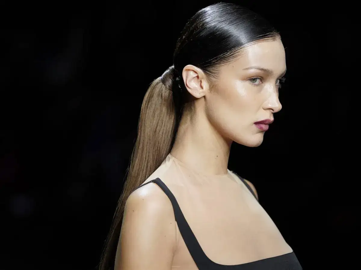 Bella Hadid con un elegante peinado de coleta alta y pelo efecto mojado, luciendo un vestido negro con escote transparente.