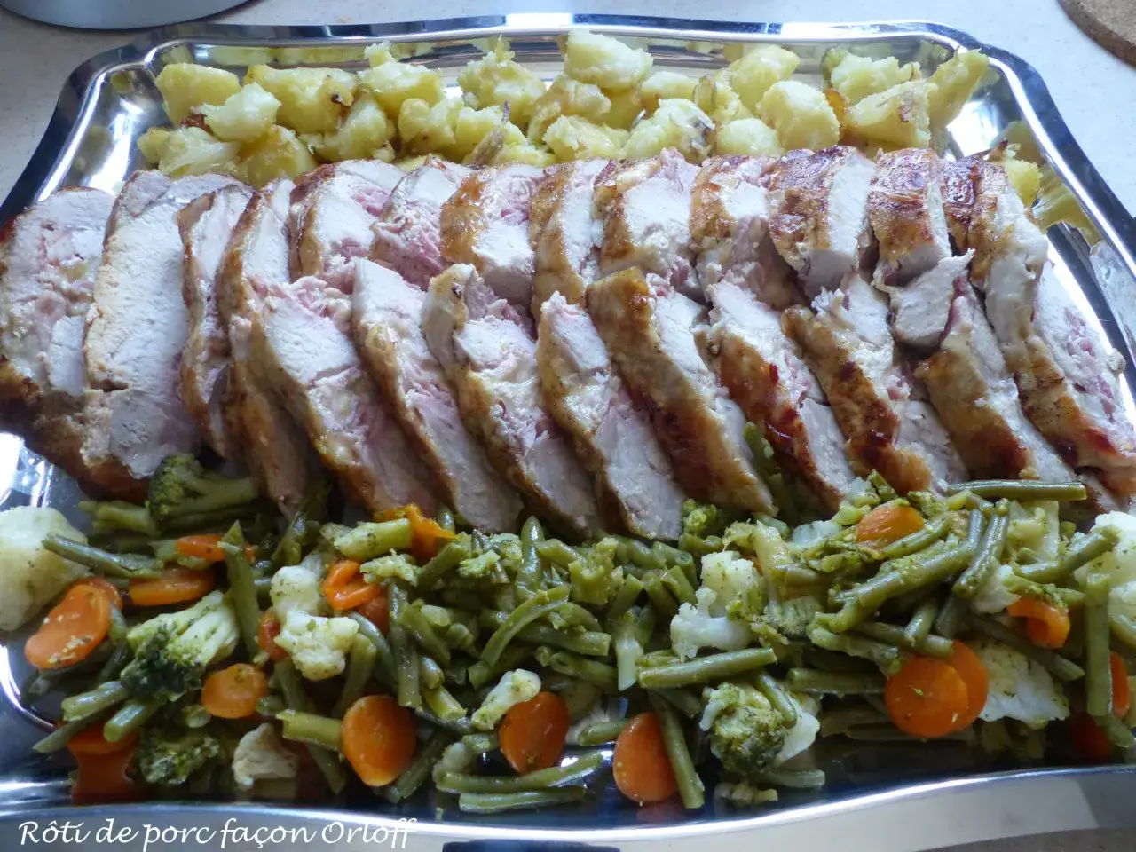 Rôti de porc Orloff tranché, servi avec des pommes de terre rôties et un mélange de légumes verts, carottes et chou-fleur.