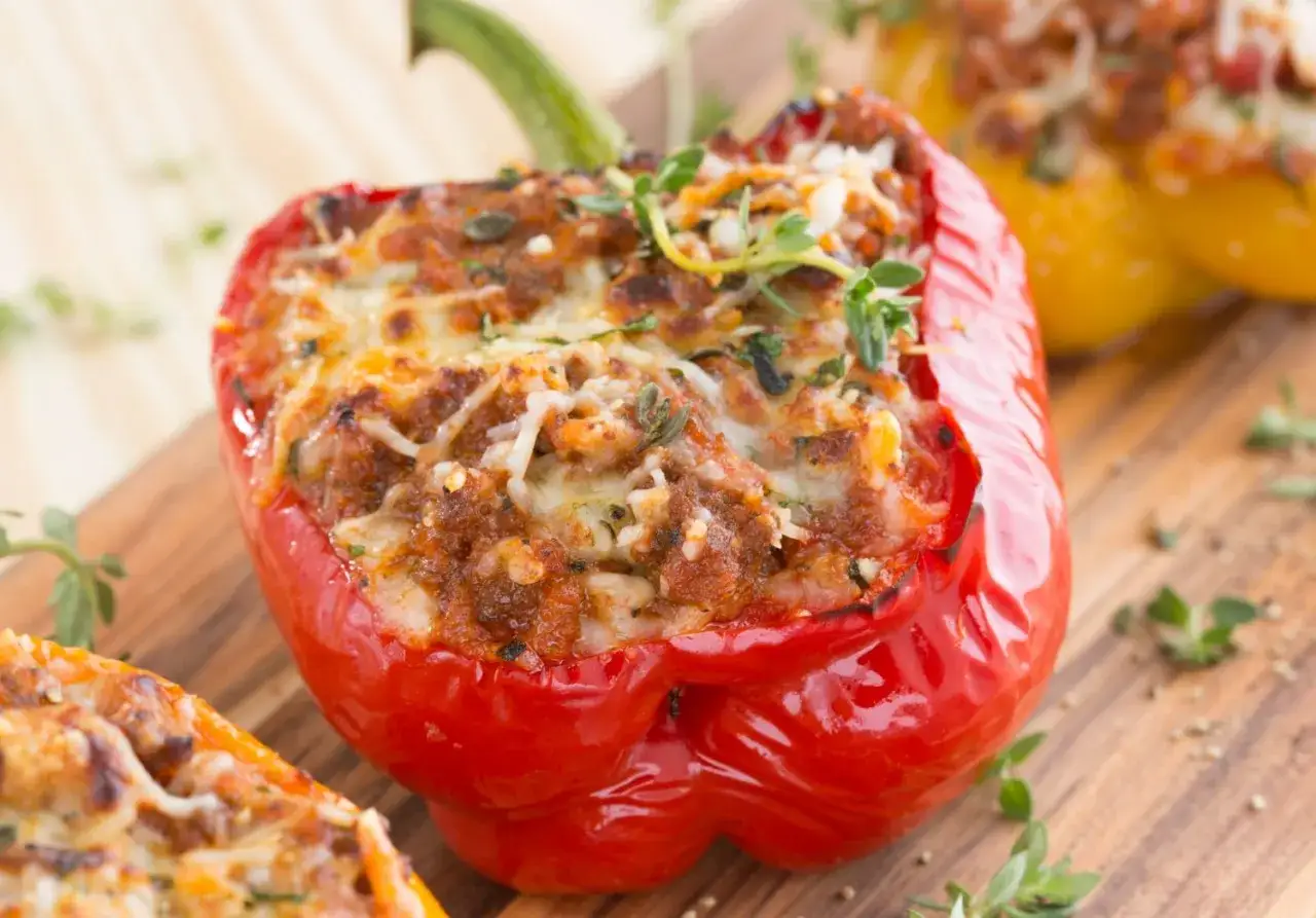 Peperoni ripieni di carne, cotti al forno e gratinati con formaggio fuso, guarniti con erbe aromatiche fresche.