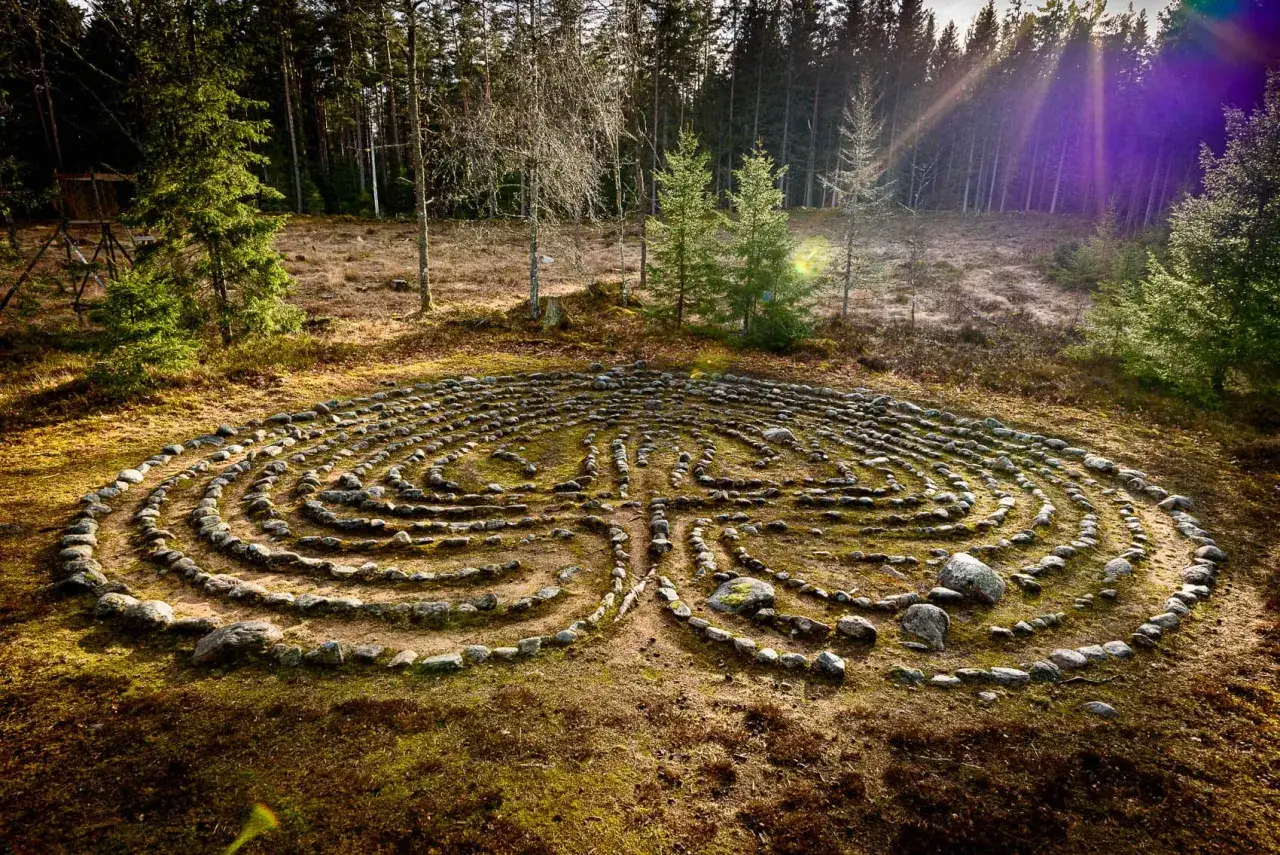En stenlagd labyrint i en svensk skog. Solstrålar bryter igenom träden och lyser upp den mossiga marken.