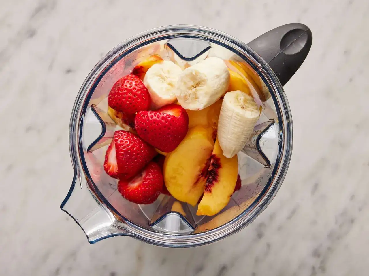 Färska jordgubbar, banan och persika i en mixer för ett härligt smoothie recept.