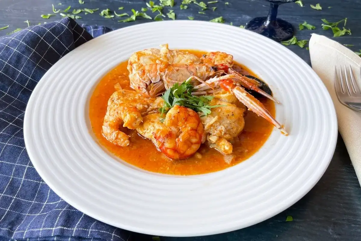 Rape en salsa con gambas y cigalas, servido en plato blanco con perejil fresco.