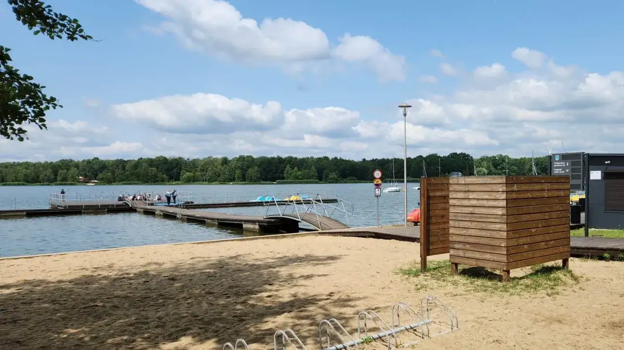 Słoneczny dzień nad jeziorem Paprocańskim w Tychach. Drewniane molo, plaża i las w tle.